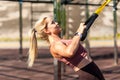 Closeup strong athlete blond woman training outdoor, pulling trx suspension straps, doing upper body workouts