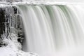 Closeup of strong waterfall flowing over ice covered cliff, smooth waters