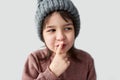Closeup studio portrait of beautiful happy little girl in the winter warm gray hat, wearing sweater and showing silent gesture and