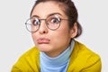 Closeup studio portrait of doubtful young woman with a bun hairstyle, wearing casual outfit and round transparent eyewear, looking