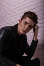 Closeup studio portrait of a young cool man with clean skin with nose piercings in a vintage black leather jacket near pink brick Royalty Free Stock Photo