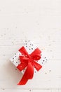 Closeup of a stylish birthday or christmas gift. Top view of a beautiful gift tied with a red gift ribbon on white table