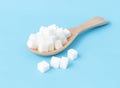 Closeup sugar cubes on wooden spoon white blue background