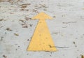 Closeup surface old and pale yellow painted arrow sign on dirty cement street floor by dried leaves textured background