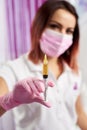 Closeup of a syringe with a liquid hold by a female professional wearing pink gloves and mask