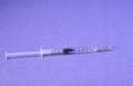 Closeup of a syringe needle with the vaccine against a purple background - COVID-