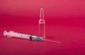 Closeup of a syringe needle with the vaccine ampoule on a red surface - COVID-19