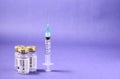 Closeup of a syringe needle with the vaccine ampoules on a purple surface - COVID-19