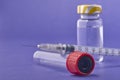 Closeup of a syringe needle with the vaccine ampoules on a purple surface - COVID-19