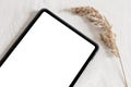 Closeup of tablet with dry grass on table. Blank, empty screen. White linen table cloth background in sunlight Royalty Free Stock Photo