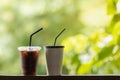 Closeup of take away plastic and paper cup of iced black coffee on wooden table with green nature background Royalty Free Stock Photo