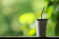 Closeup of takeaway paper cup of iced coffee with plastic cover and straw on wooden table with green nature background and copy Royalty Free Stock Photo