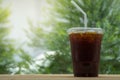 Closeup of takeaway plastic cup of iced black coffee Americano on wooden table with copy space