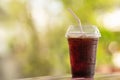 Closeup of takeaway plastic cup of iced black coffee Americano on wooden table with green nature background Royalty Free Stock Photo