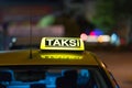 Closeup of a [taksi-taxi] sign on the car under the lights in the night with a blurry background