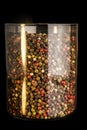 closeup tall glass jar with mix of different peppercorns