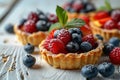 closeup of tartlets with fresh different berries, bakery dessert with sweet blueberry, raspberry and mint leaves on white wooden