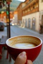 Closeup Texture of Half Cup of Hot Cappuccino Coffee in Woman`s Hand against Blurry Old Town Royalty Free Stock Photo