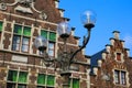 Closeup of three armed old street lamp with typical belgian stepped gable house facade background against blue sky