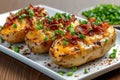 Closeup three baked potatoes stuffed with bacon, green onions and cheddar cheese on white plate, delicious snack