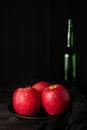 Closeup of three red apples on plate, wooden table with green bottle Royalty Free Stock Photo