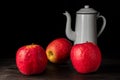 Closeup of three red apples on wooden table with white vintage coffee pot, black background Royalty Free Stock Photo