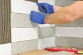 Closeup of tiler hand laying ceramic tile on wall in kitchen, renovation, repair, construction