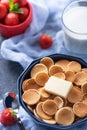 Closeup tiny cereal pancakes with slice of butter, strawberries, glass of milk on blue background, rural Breakfast