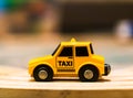 Closeup of a tiny taxi car toy on a wooden table on a blurry background