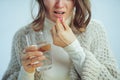 Closeup on tired woman with cup of water eating pill