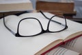 Closeup to a black glasses over a blank book over a literature book and old books at background