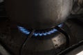 Closeup to a dirty natural gas stove on with dirty cocoa cooking pot over a flame.