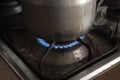 Closeup to a dirty natural gas stove on with dirty cocoa cooking pot over a flame.