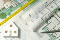Closeup to floor plans, white paper house and measuring yellow tape. Architect drawings, expensive renovation, buildings