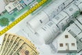 Closeup to floor plans, white paper house, measuring yellow tape and US dollars. Architect drawings, expensive renovation