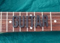Closeup to a GUITAR lettering black word over a six electric guitar strings and wooden fretboard over a green background Royalty Free Stock Photo