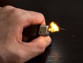Closeup to a male hand holding a yellow lighter with flame over a dark wooden table Royalty Free Stock Photo