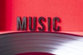 Closeup to a MUSIC black lettering word over a red background and a black LP vinyl Royalty Free Stock Photo