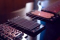 Closeup to a six black electric guitar strings, wooden fretboard and microphones iluminated with red ligths