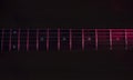 Closeup to a six black electric guitar strings and wooden fretboards iluminated with red lights