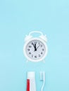 Closeup of a toothpaste, toothbrush and white alarmclock on blurred blue background. Teeth or dentures concept on blue background