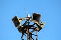 Closeup of top of tall strong metal structure holding four large public civil defence warning air sirens