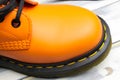 Closeup top view on bright orange color tip of one single leather boot, black sole, yellow stitching on white wood background Royalty Free Stock Photo