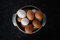 Closeup top view of handmade ceramic bowl of fresh organic brown and white eggs on dark moody background. Royalty Free Stock Photo