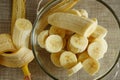 Closeup top view of pile of banana slices and a half of a banana fruit in a glass bowl and a peeling banana on side