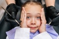 Closeup top view portrait of cute afraid child girl holding head from fear with hand, sitting on dentist chair. Close-up Royalty Free Stock Photo