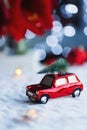 Closeup toy car with Christmas tree on the roof indoor with red home festive decor and blurred bokeh background in daylight Royalty Free Stock Photo