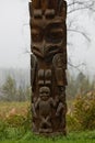 Closeup of traditional carved Gitxsan totem poles with mist covered forest behind