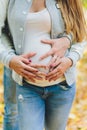 Closeup on tummy of pregnant woman, wearing long green dress, holding in hands bouquet of daisy flowers outdoors, new Royalty Free Stock Photo