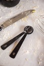 Closeup of two black measuring spoons and a knife on a table covered in flour. Royalty Free Stock Photo